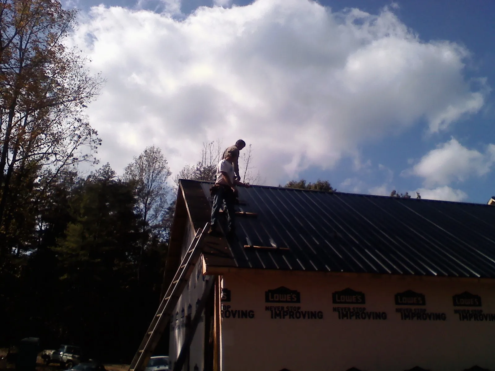 Roofer fastening dark metal panels high against a cloudy sky, from a Roof Inspection job in Parsons