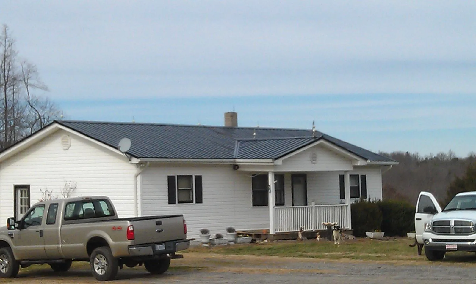 Finished dark metal roof on a white ranch home with work trucks parked in Parsons