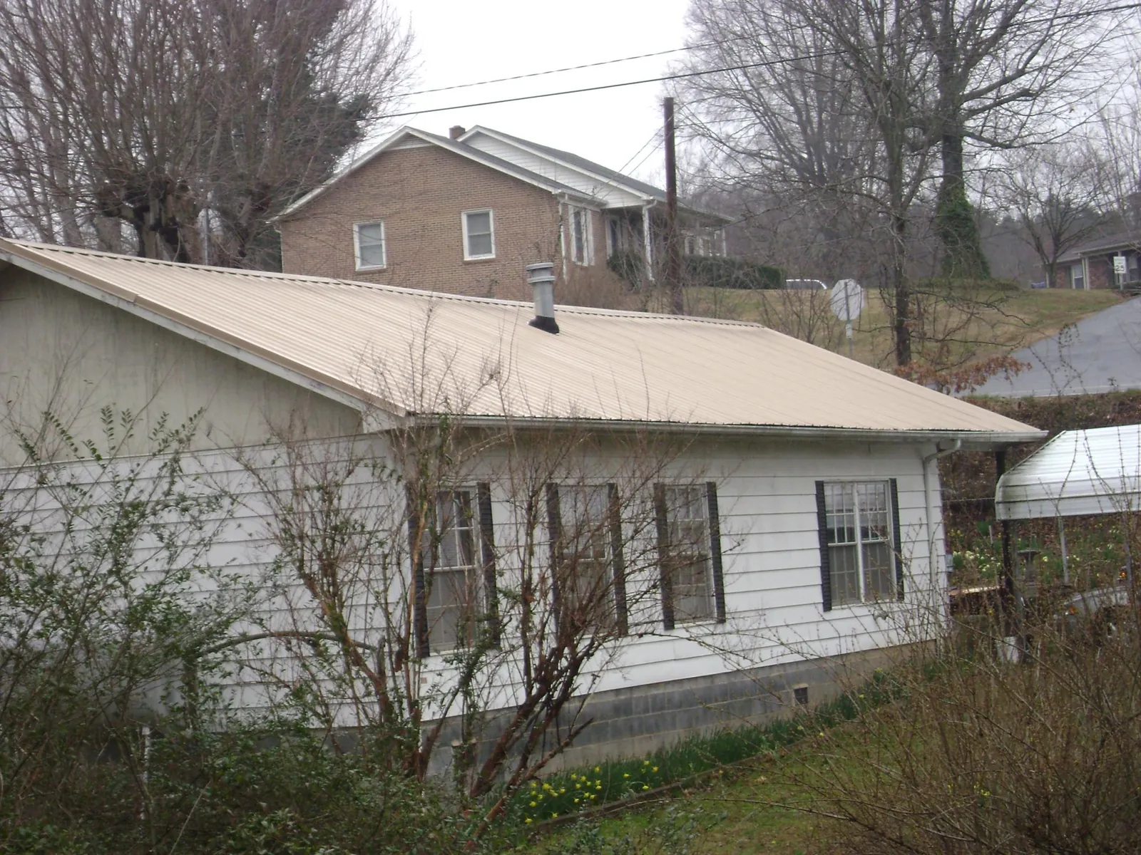 Tan metal roof on a white sided house set into a hillside — Commercial Roofing by Roofing Brothers in Parsons